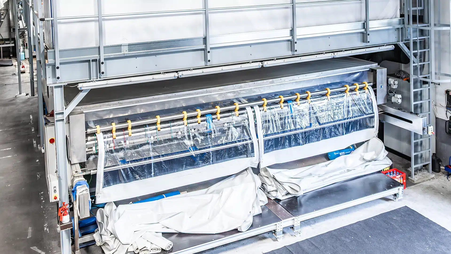 Unternehmen 5 Maschine mit Folienrolle in einer industriellen Umgebung, umgeben von Metallrahmen und Stauraum für Materialien.